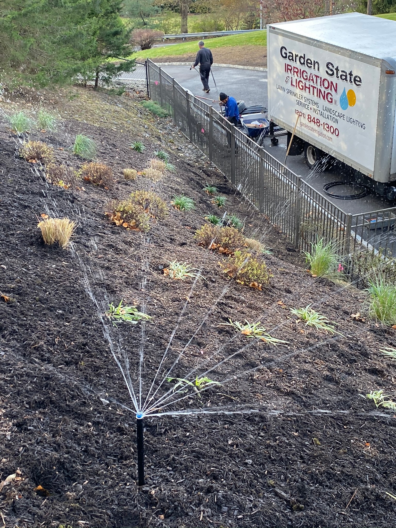 Sprinkler watering a sloped planting bed beside the Garden State truck