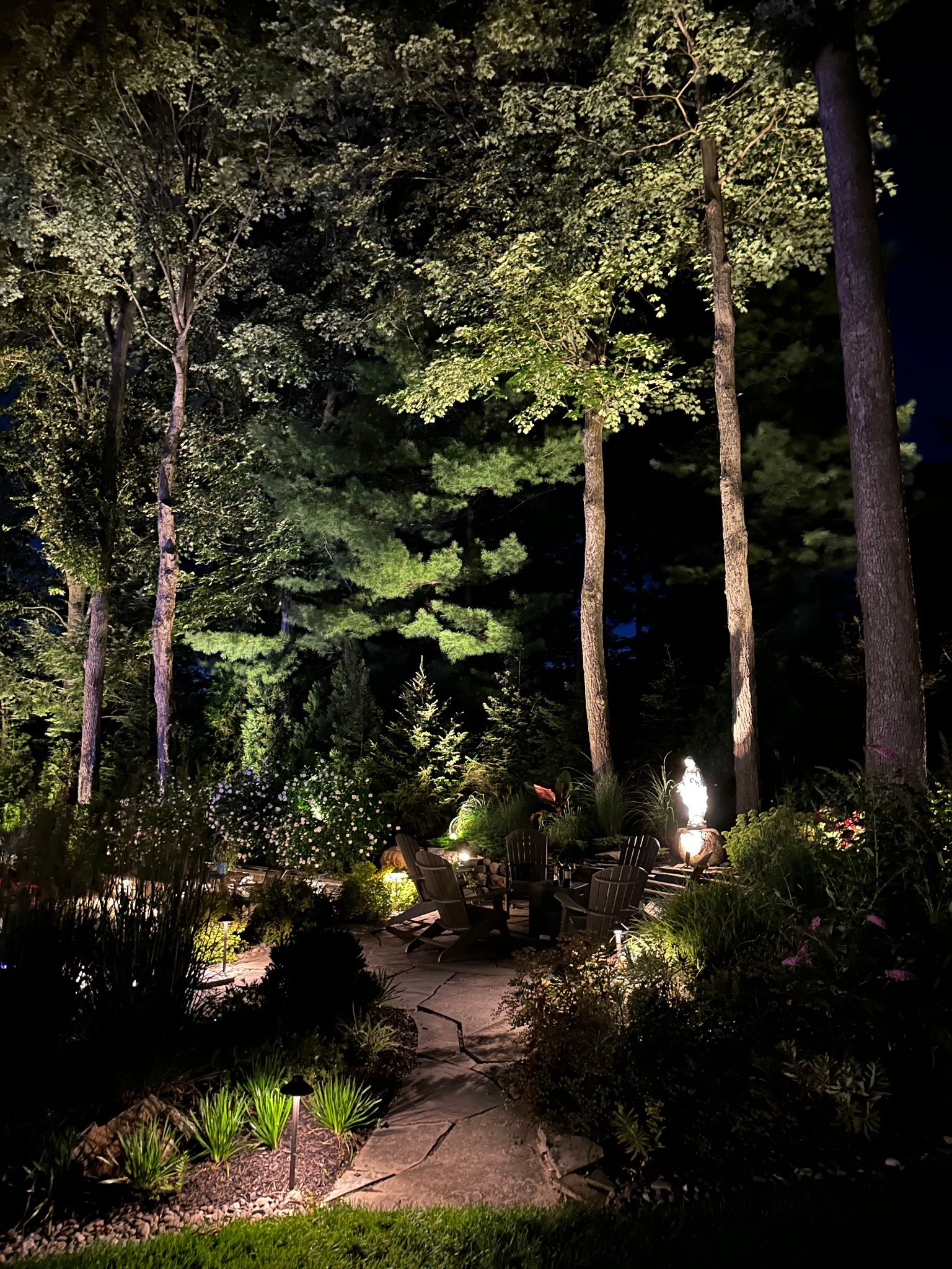 A garden walkway surrounded by illuminated planting beds and trees