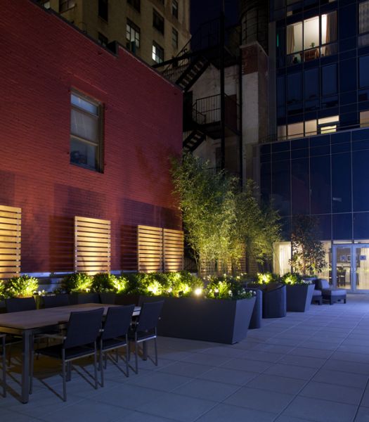 Illuminated planter beds and architectural lighting beside a courtyard dining area